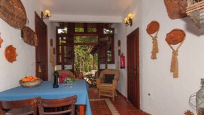 A dining area with a table set for two, a wicker chair, and a view through a doorway to an outdoor space. - GC0004 Cosy cave cottage & private jacuzzi in Fontanales (Moya)