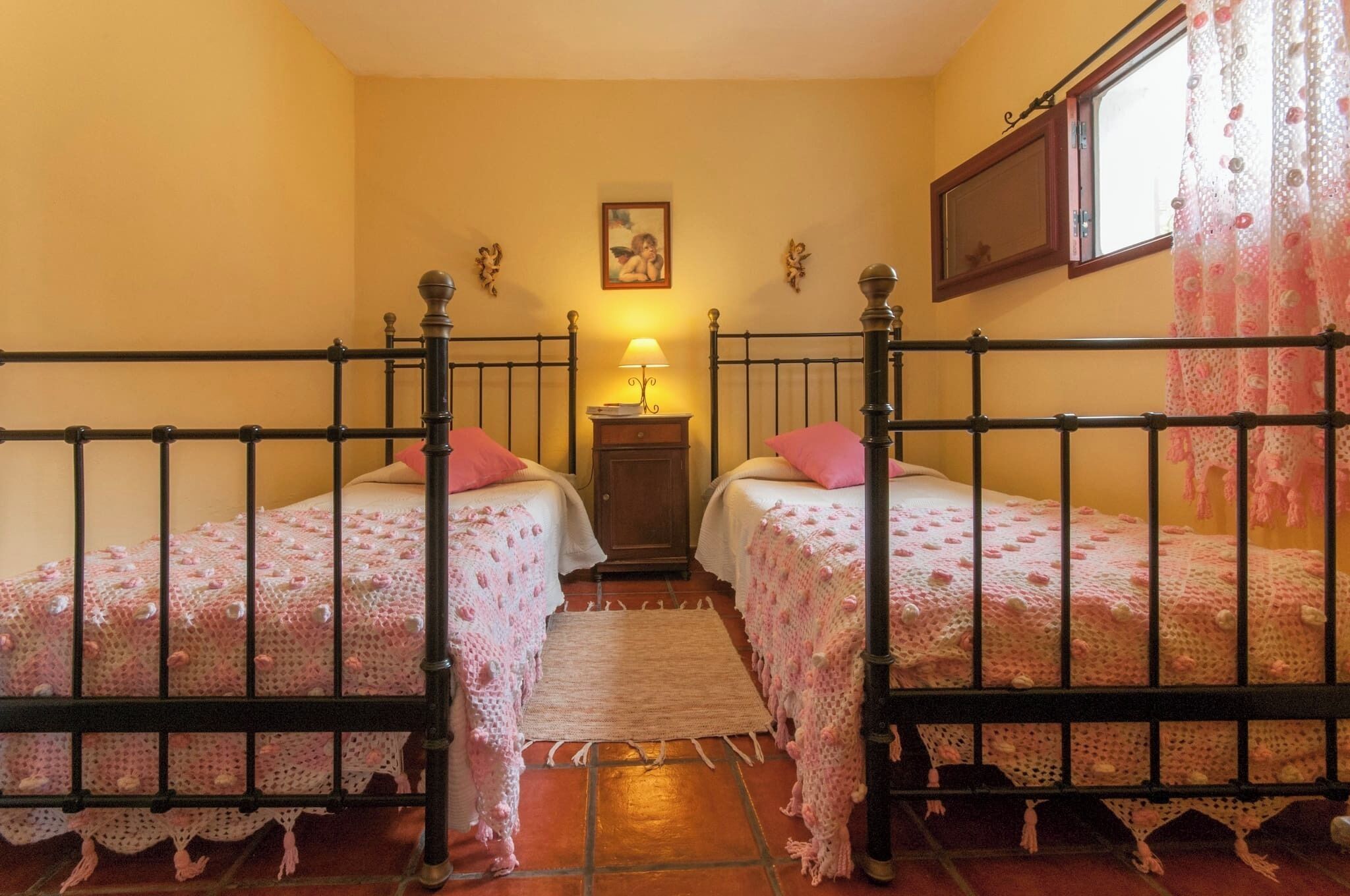 A room with two beds, a small table with a lamp, and a window with curtains.