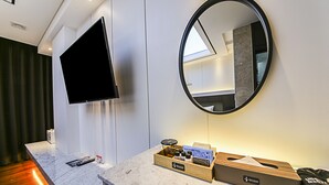 A modern hotel room with a marble countertop, a flat-screen TV, a round mirror, and a wooden tray with toiletries. - Hotel Artheim (Gwangju)