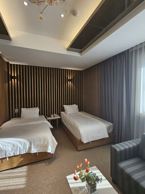 A modern hotel room with two beds, a small table with a vase of flowers, and a sofa. - Hotel Artheim (Gwangju)