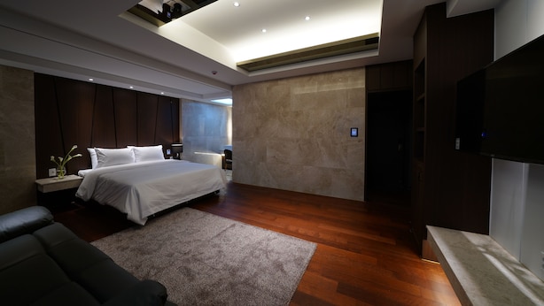 A modern bedroom with a large bed, a flat-screen TV, and a wooden floor. - Hotel Artheim (Gwangju)