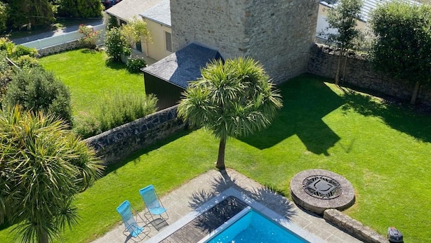 A swimming pool with a white umbrella, surrounded by a stone wall, with a view of a castle-like building in the background. - Villa Tourelle (Dinan)