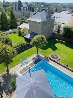 A swimming pool with a white umbrella, surrounded by a stone wall, with a view of a castle-like building in the background. - Villa Tourelle (Dinan)