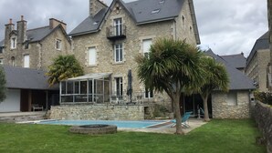 A stone building with a swimming pool, a covered patio, and a well-maintained lawn. - Villa Tourelle (Dinan)