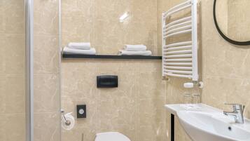 Un baño moderno con cabina de ducha de vidrio, inodoro, lavabo y perchero para toallas.