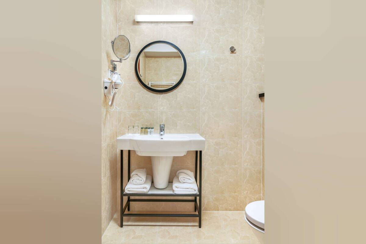 A bathroom with a white sink, a round mirror, and a towel rack.