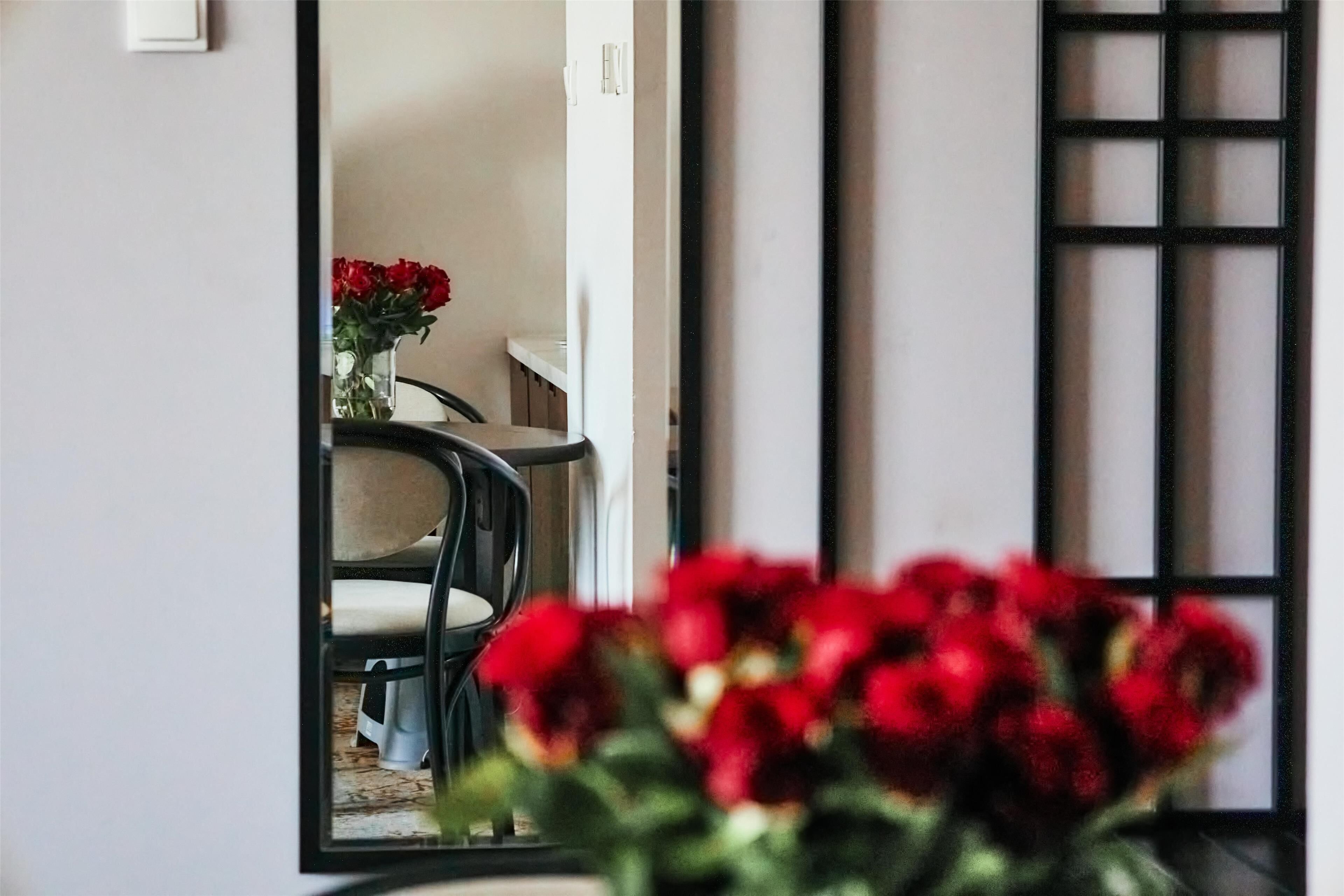 Una habitación con una mesa de comedor y sillas, un florero con flores rojas y una puerta corrediza con un diseño de cuadrícula.