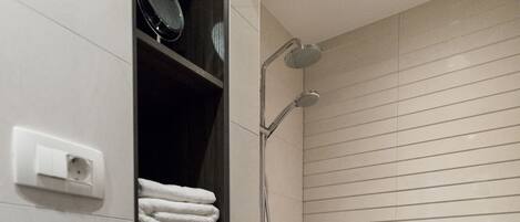 A modern bathroom with a glass-enclosed shower, a built-in shelf with folded towels, and a wall-mounted mirror.