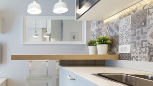 A modern kitchen with a white countertop, stainless steel sink, and a potted plant on the backsplash.