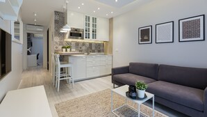 A modern living room with a grey sofa, a white coffee table, and a kitchen area with white cabinets and a microwave.
