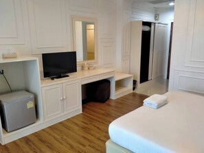 Habitación de hotel con cama, televisión, refrigerador pequeño, espejo y armario.