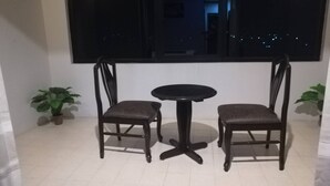 Una habitación pequeña con una mesa redonda y dos sillas, una ventana y dos plantas en macetas.
