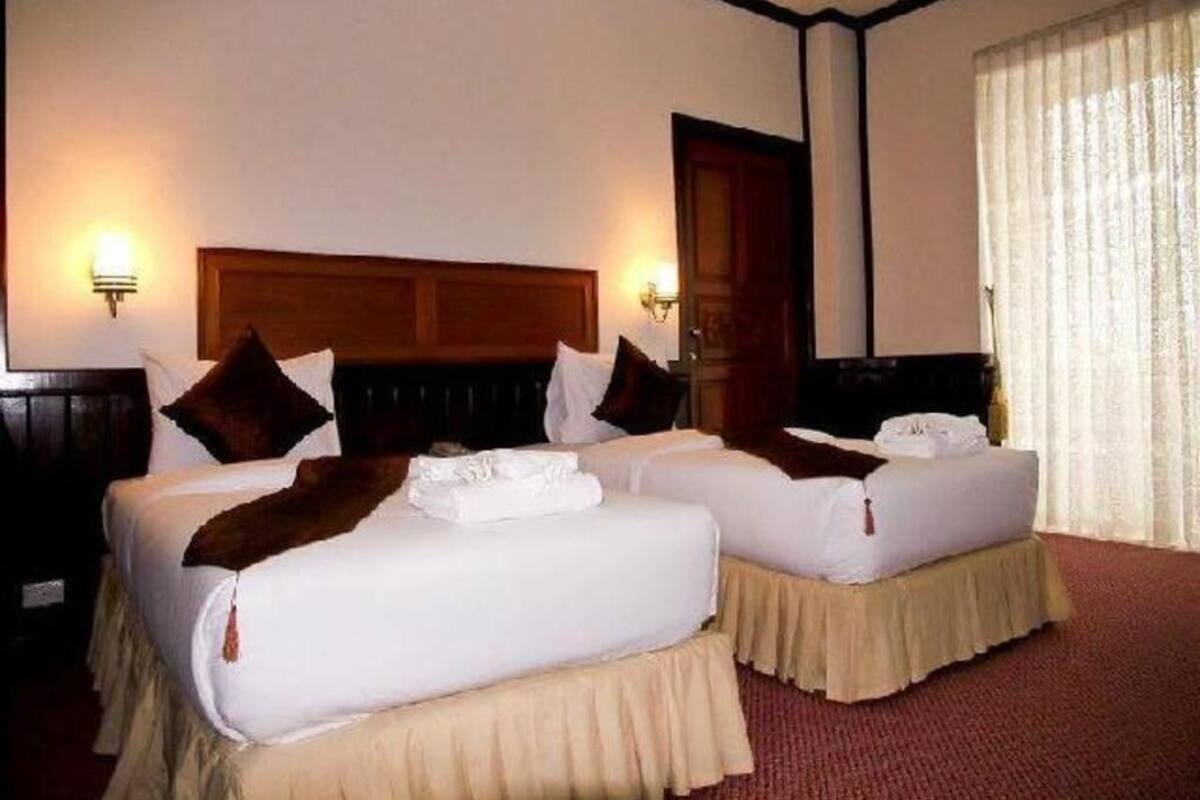 Ein Hotelzimmer mit zwei Betten, einem Holzkopfende und einem großen Fenster mit Vorhängen.