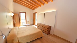 Une chambre à coucher comprenant un lit, une commode en bois, un ventilateur et une porte donnant sur un balcon.