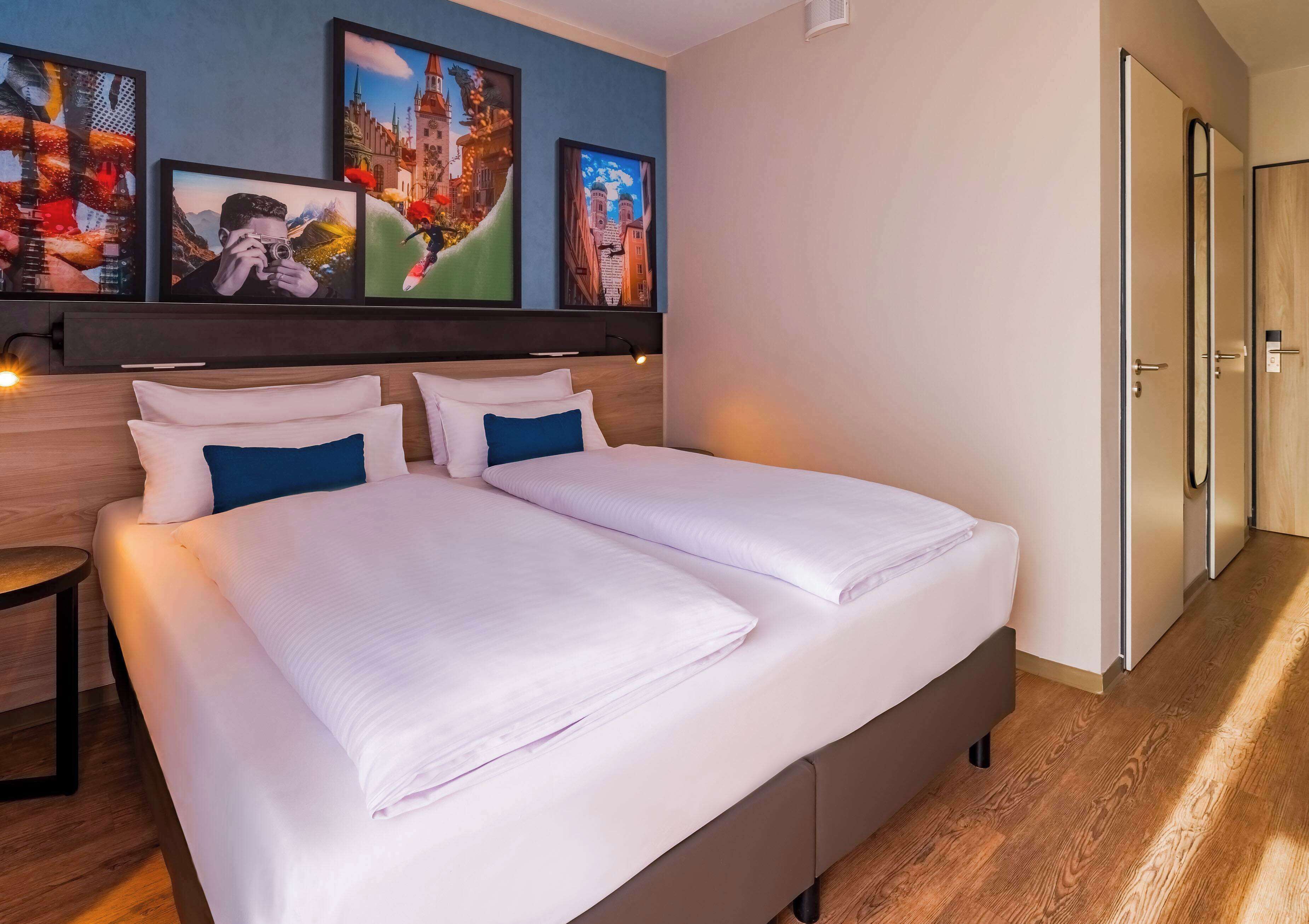 Ein Hotelzimmer mit Doppelbett, zwei Kissen, einem Kopfteil und drei gerahmten Kunstwerken an der Wand.