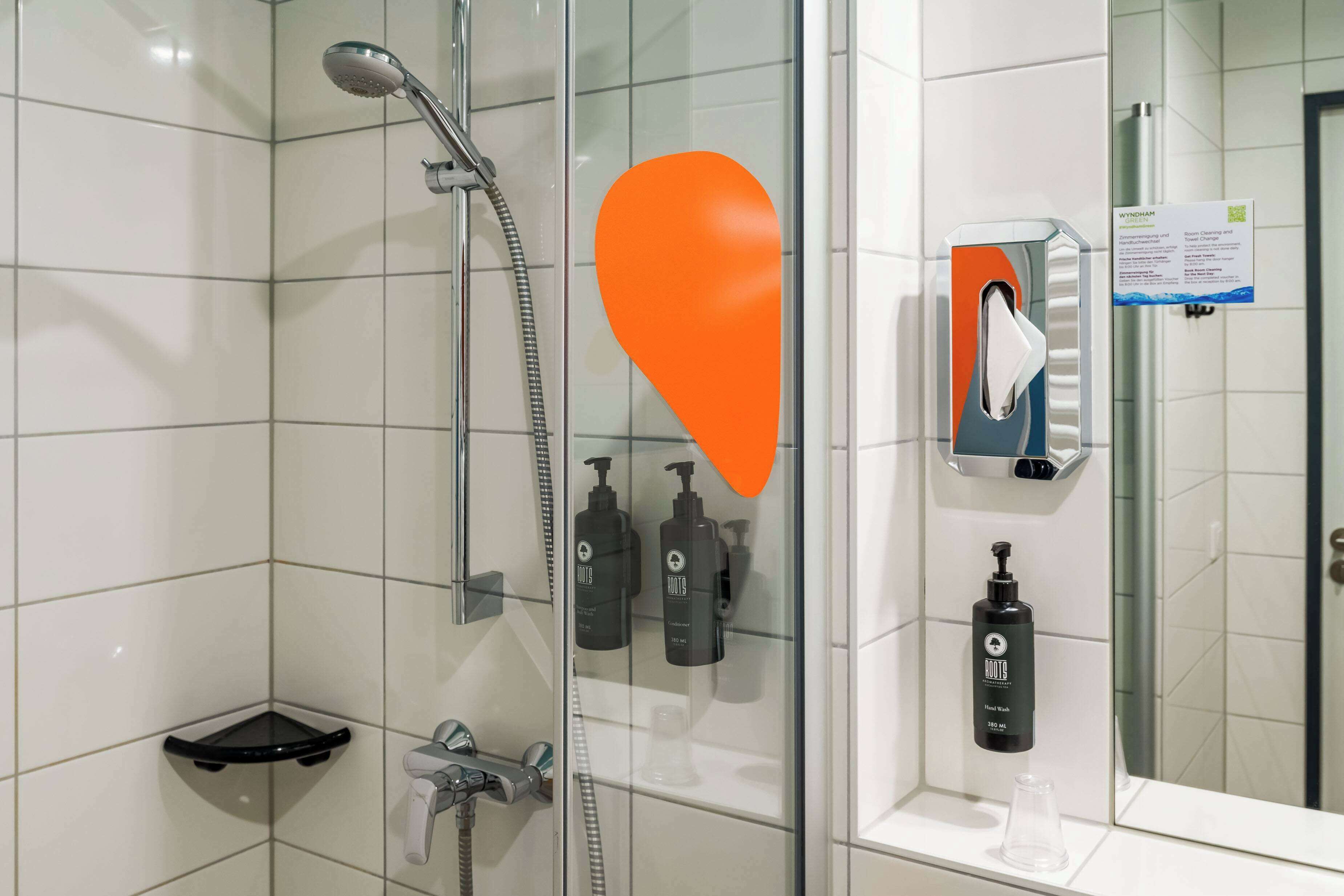 A modern bathroom with a glass shower enclosure, a handheld showerhead, a soap dispenser, and a small shelf.