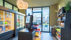 Interior moderno de un supermercado con secciones refrigeradas, una caja registradora y vistas al estacionamiento a través de grandes ventanales.