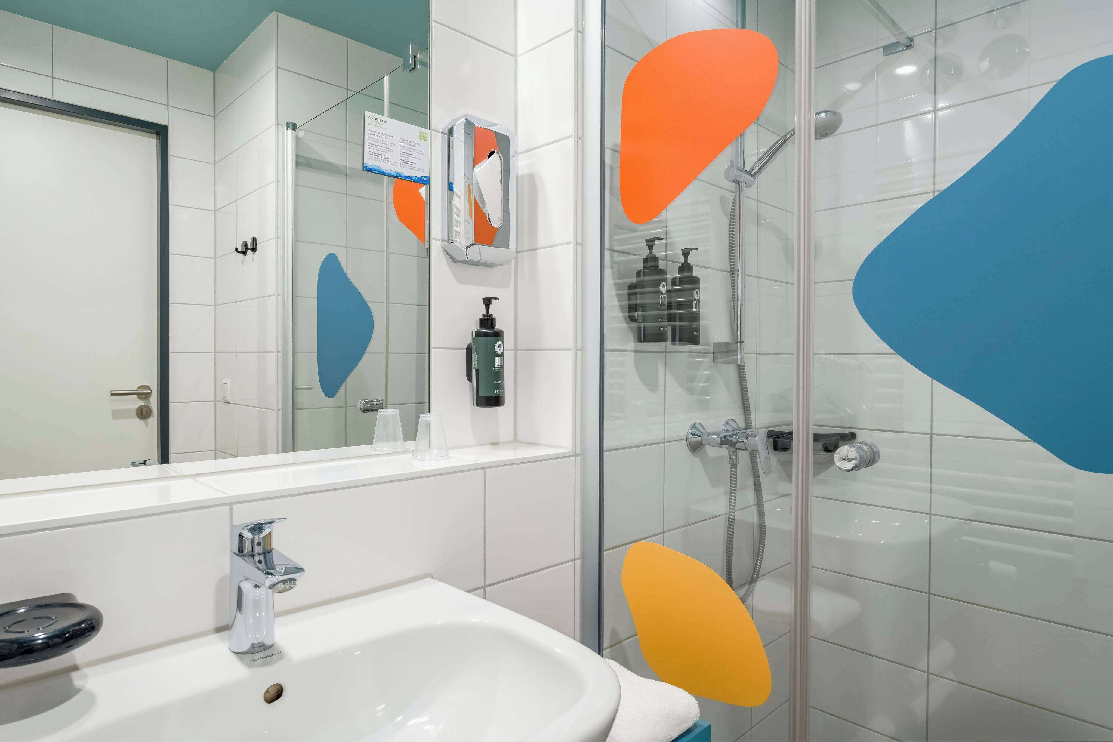 Un baño moderno con un lavamanos blanco, cabina de ducha de vidrio y un espejo que refleja la habitación.