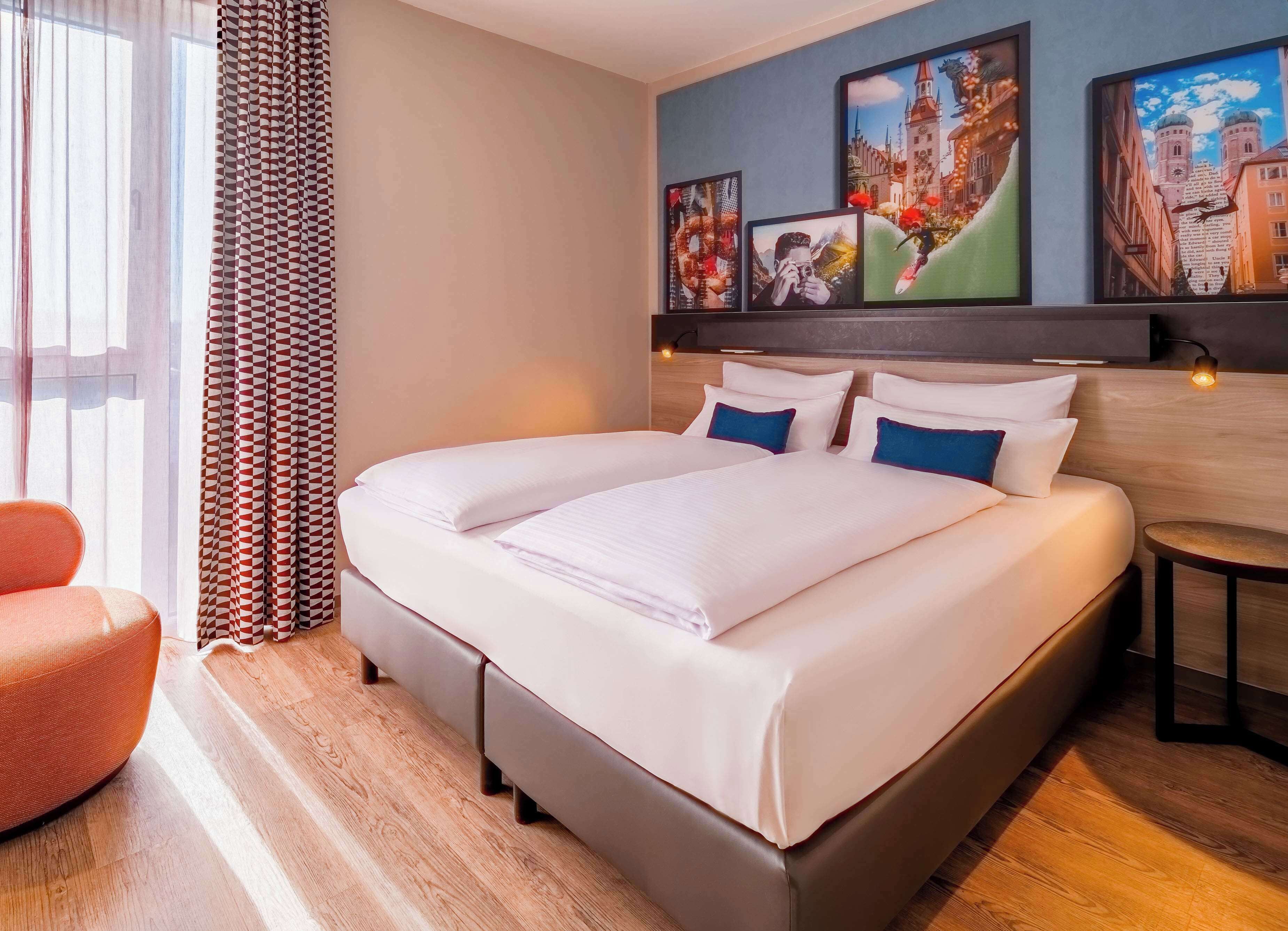 A hotel room with a large bed, two pillows, a nightstand, a chair, and artwork on the wall.