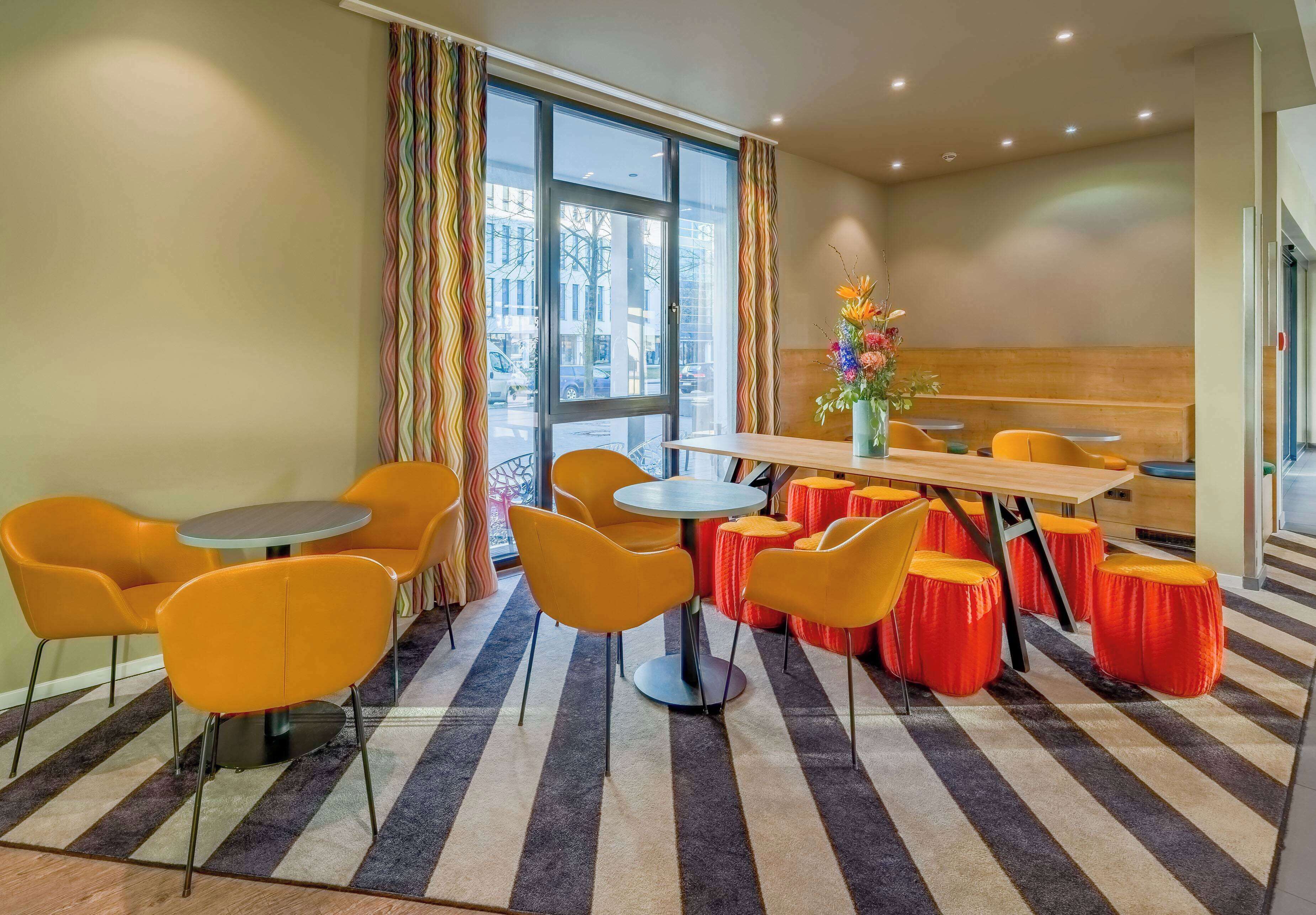 Un área de comedor con una mesa redonda y sillas anaranjadas, un banco de madera y una cortina colorida.