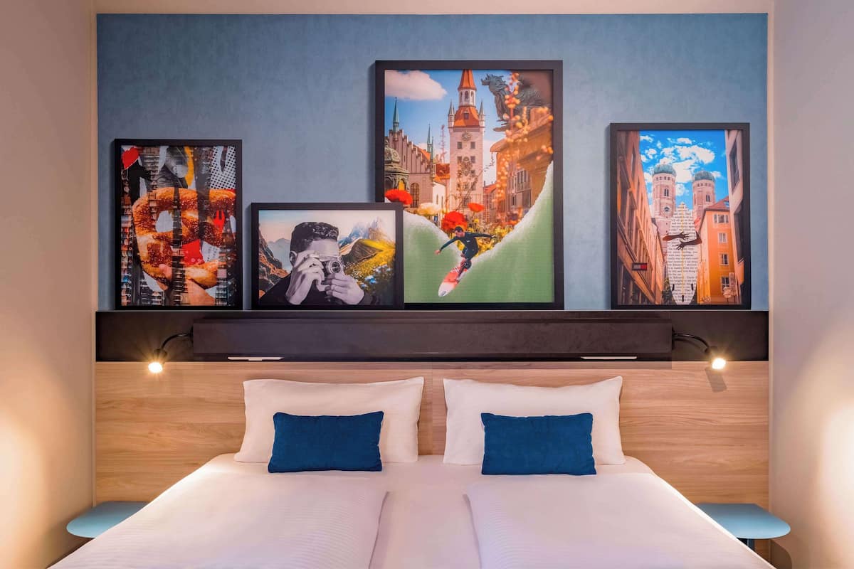 A hotel room with a large bed, two pillows, and a headboard with wall art.