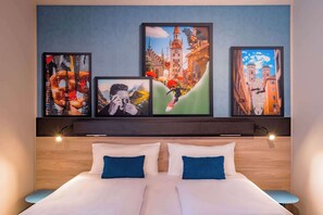 Habitación de hotel con una cama grande, dos almohadas y cabecera decorada con arte en la pared.