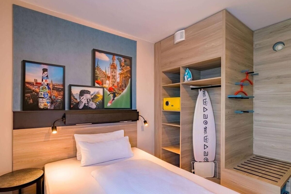 Una habitación de hotel con cama, mesita de noche, estante empotrado con adornos y armario integrado con espejo y compartimentos guardado.