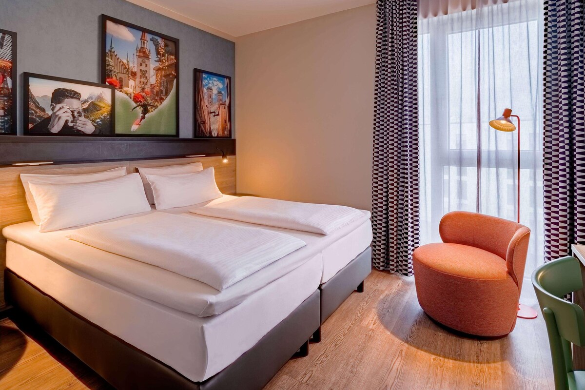 Una habitación de hotel con una cama grande, una silla y una obra de arte en la pared.