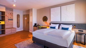 Una habitación de hotel moderna con una cama grande, un escritorio, un espejo y una obra de arte colgada en la pared.