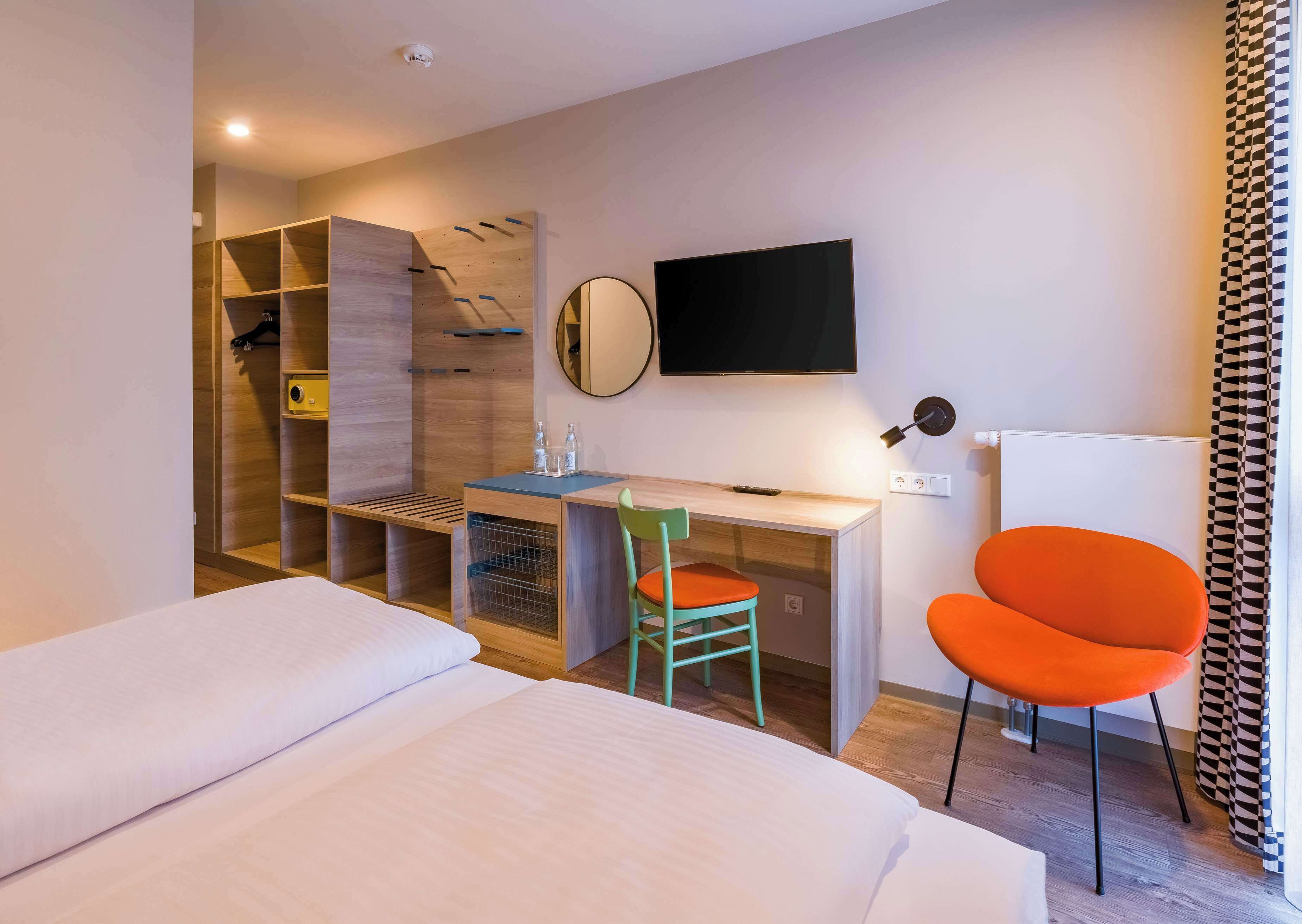A hotel room with a bed, a desk with a chair, a TV, and a wardrobe.