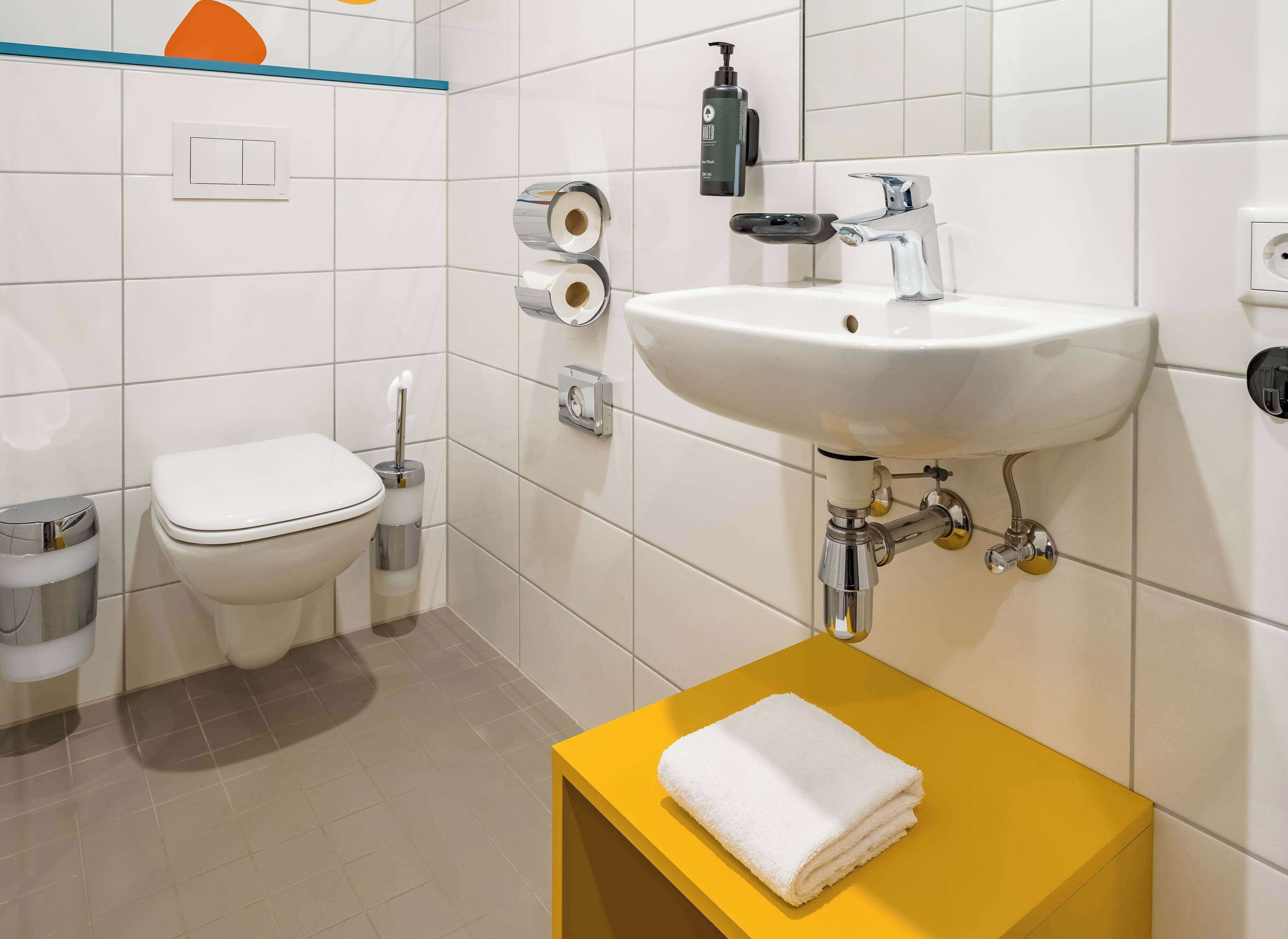 A modern bathroom with a white sink, toilet, and a yellow vanity with a towel.