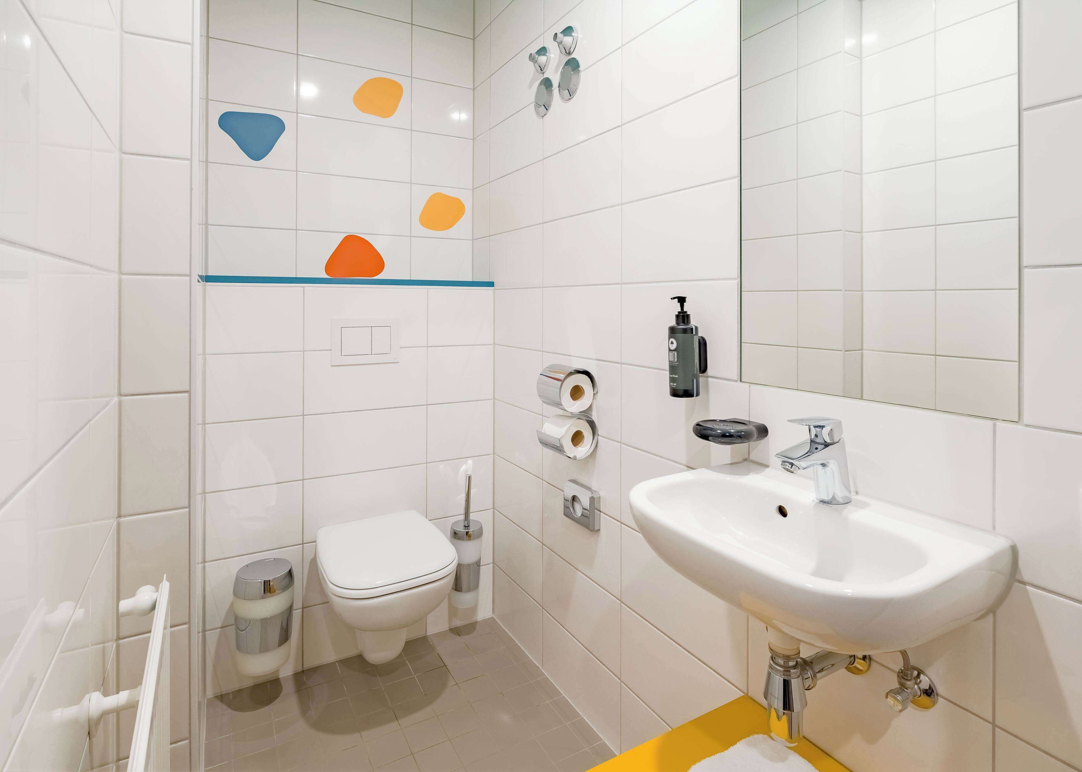 Une salle de bain moderne avec des carreaux blancs, des toilettes, un lavabo et une douche.