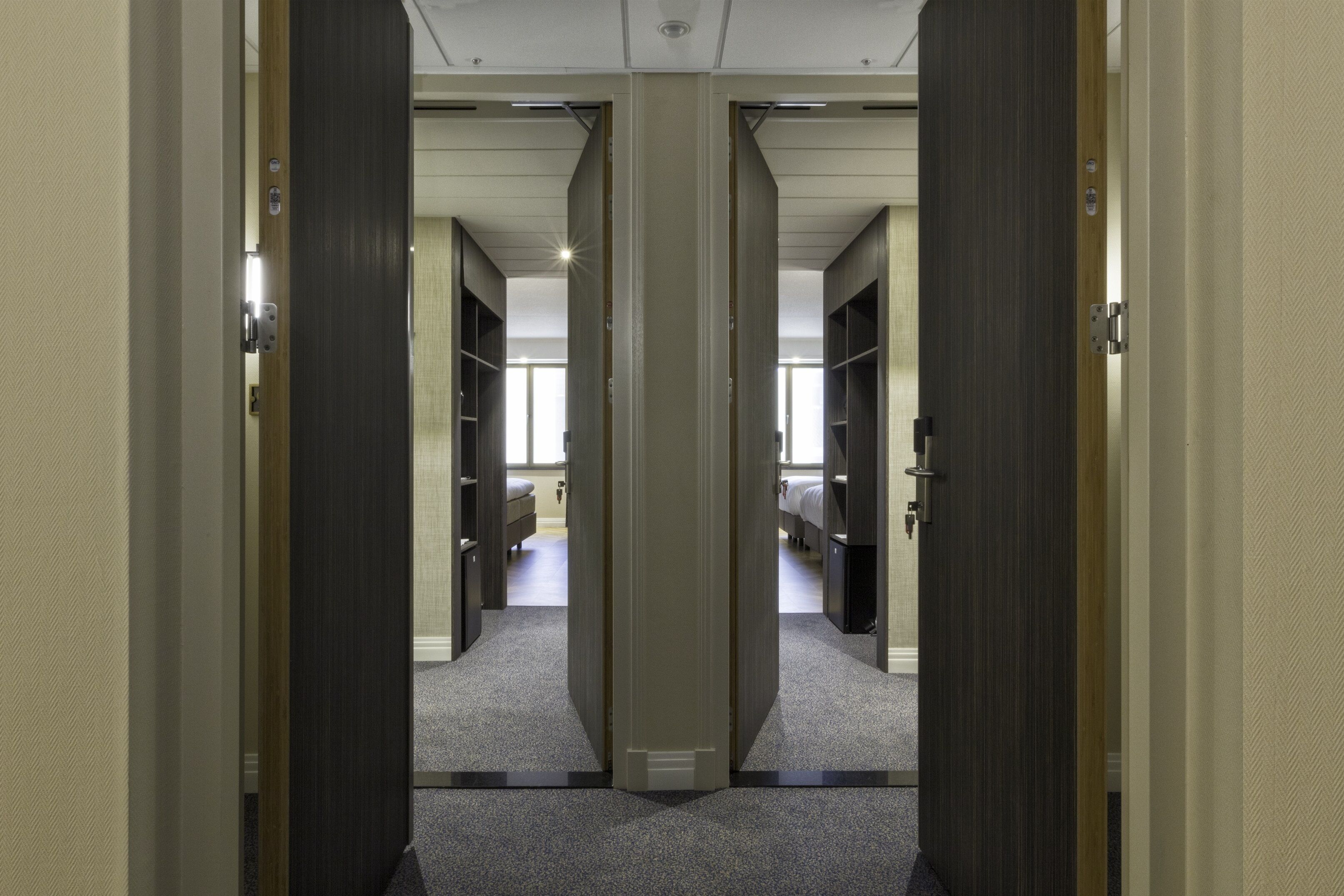 A hallway with mirrored doors leading to a room with a bed and a desk.