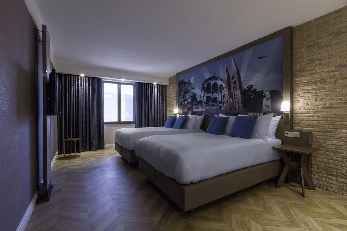 Ein Hotelzimmer mit zwei Betten, einem großen Gemälde an der Wand, einem Fernseher und einem kleinen Tisch.