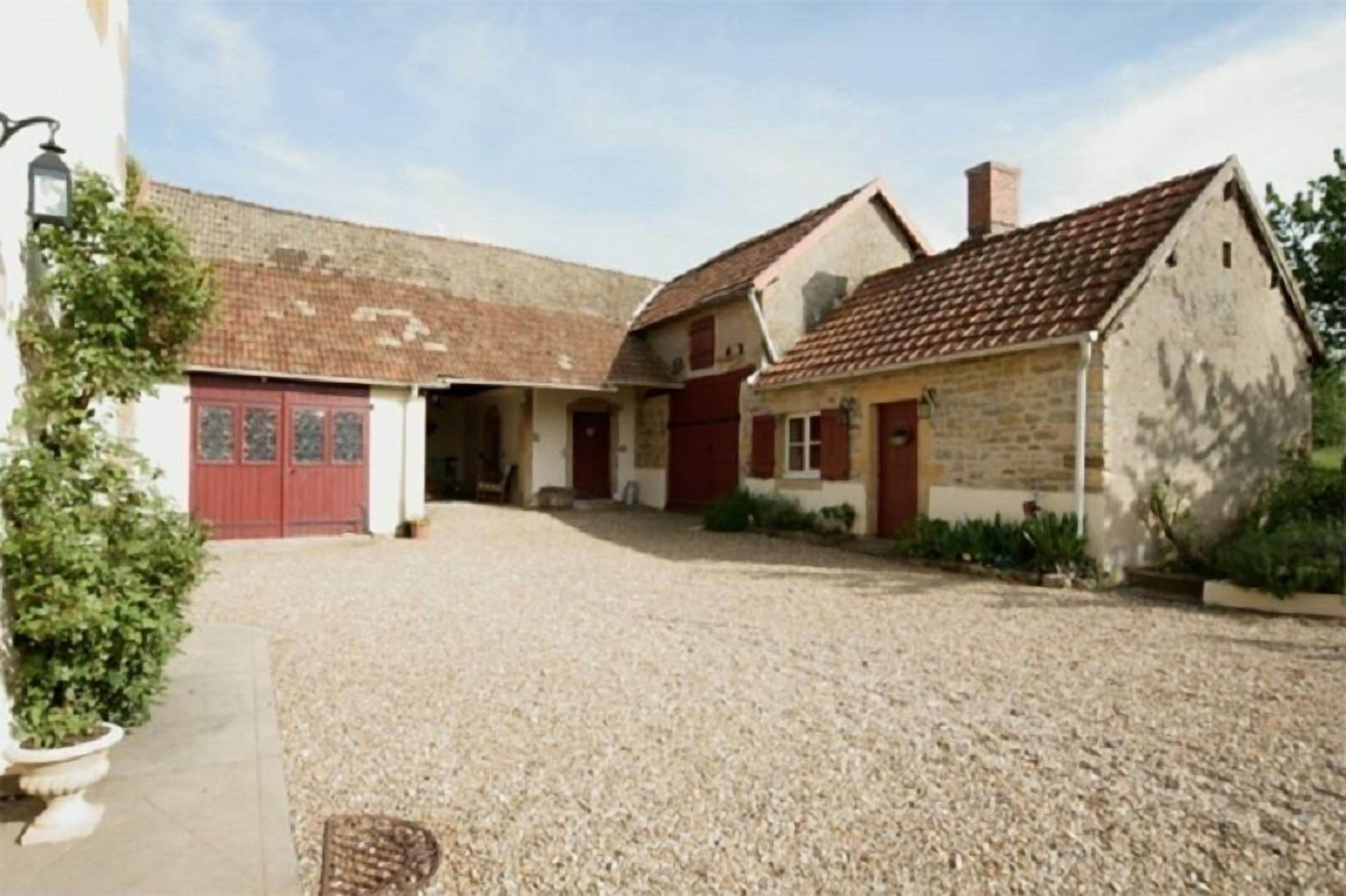 Un bâtiment avec une allée gravillonnée, une porte rouge et une façade en pierre.