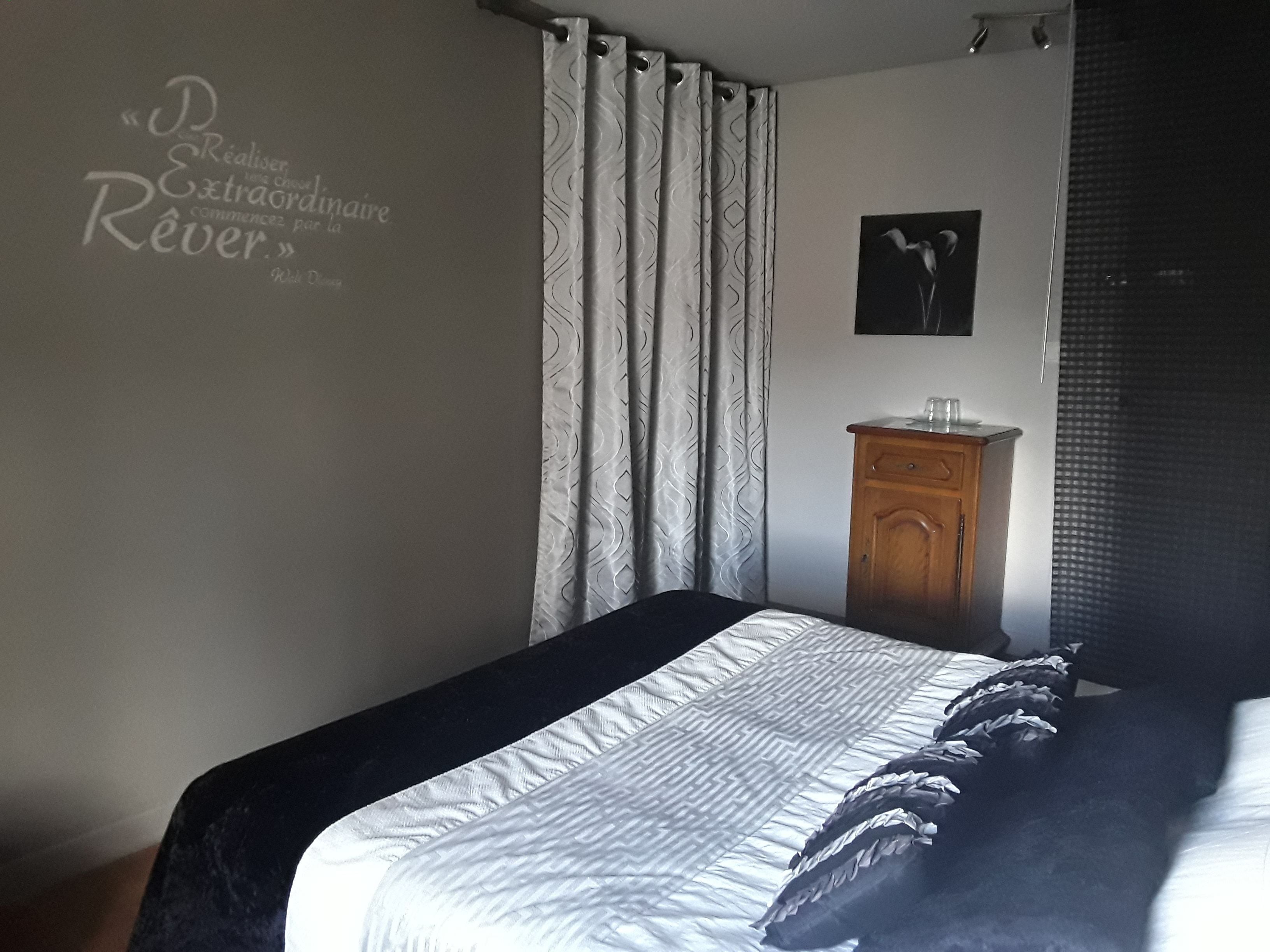 Un dormitorio con una cama, un aparador de madera, una pared con una cita y una ventana con cortinas.