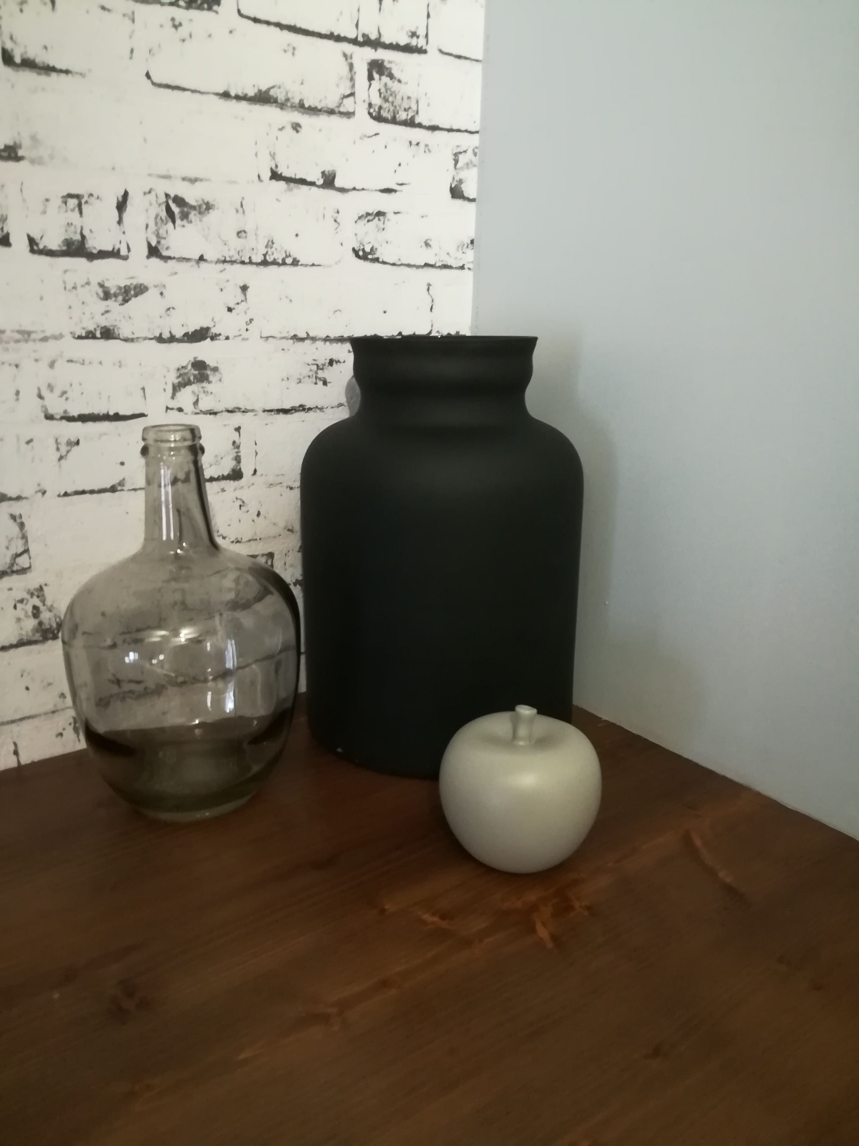 A wooden table with a clear glass bottle, a black vase, and a white ceramic object.