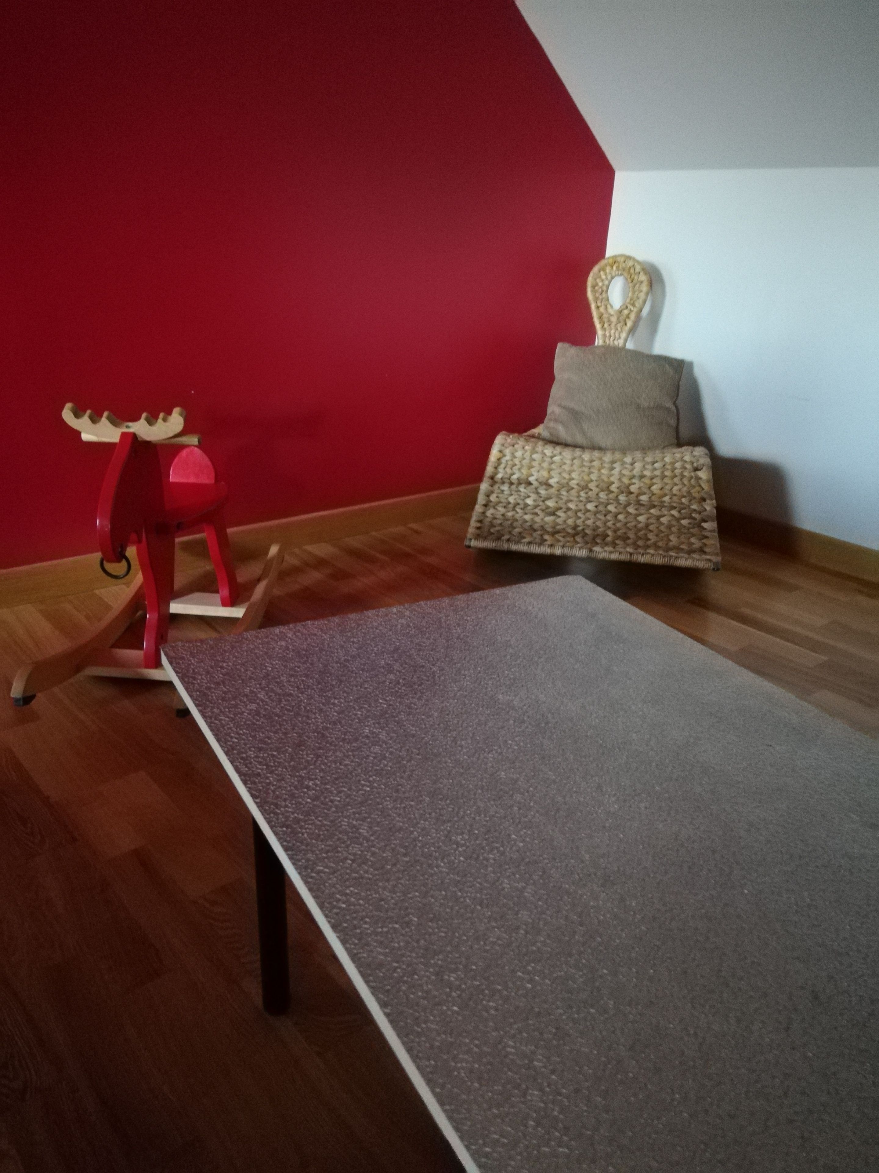 Een kamer met een houten vloer, een grijs tapijt, een rode muur, een schommelstoel en een geweven stoel.