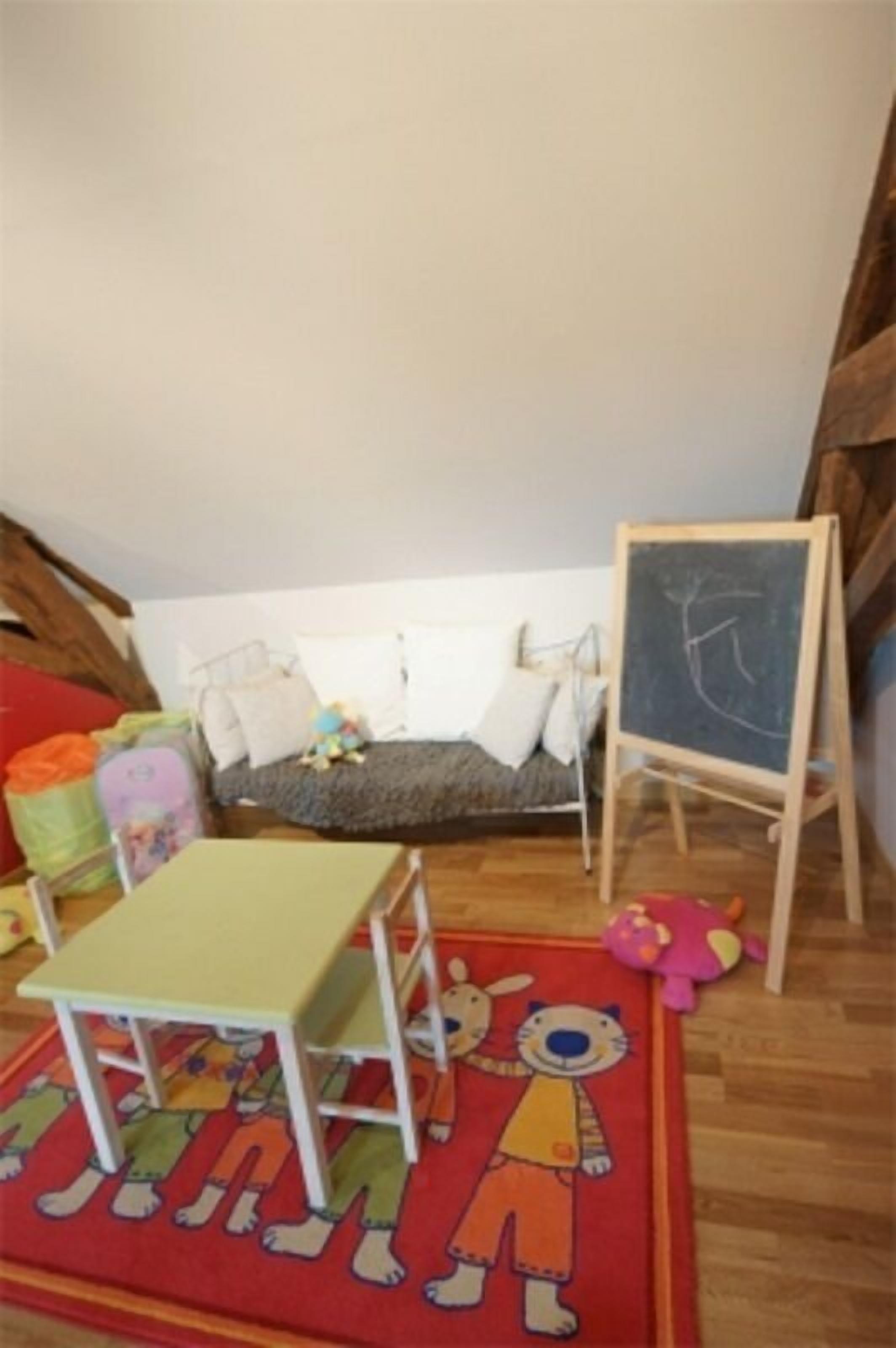 Een kinderspeelkamer met een kleine tafel, een bank, een schoolbord en een kleurrijk vloerkleed.