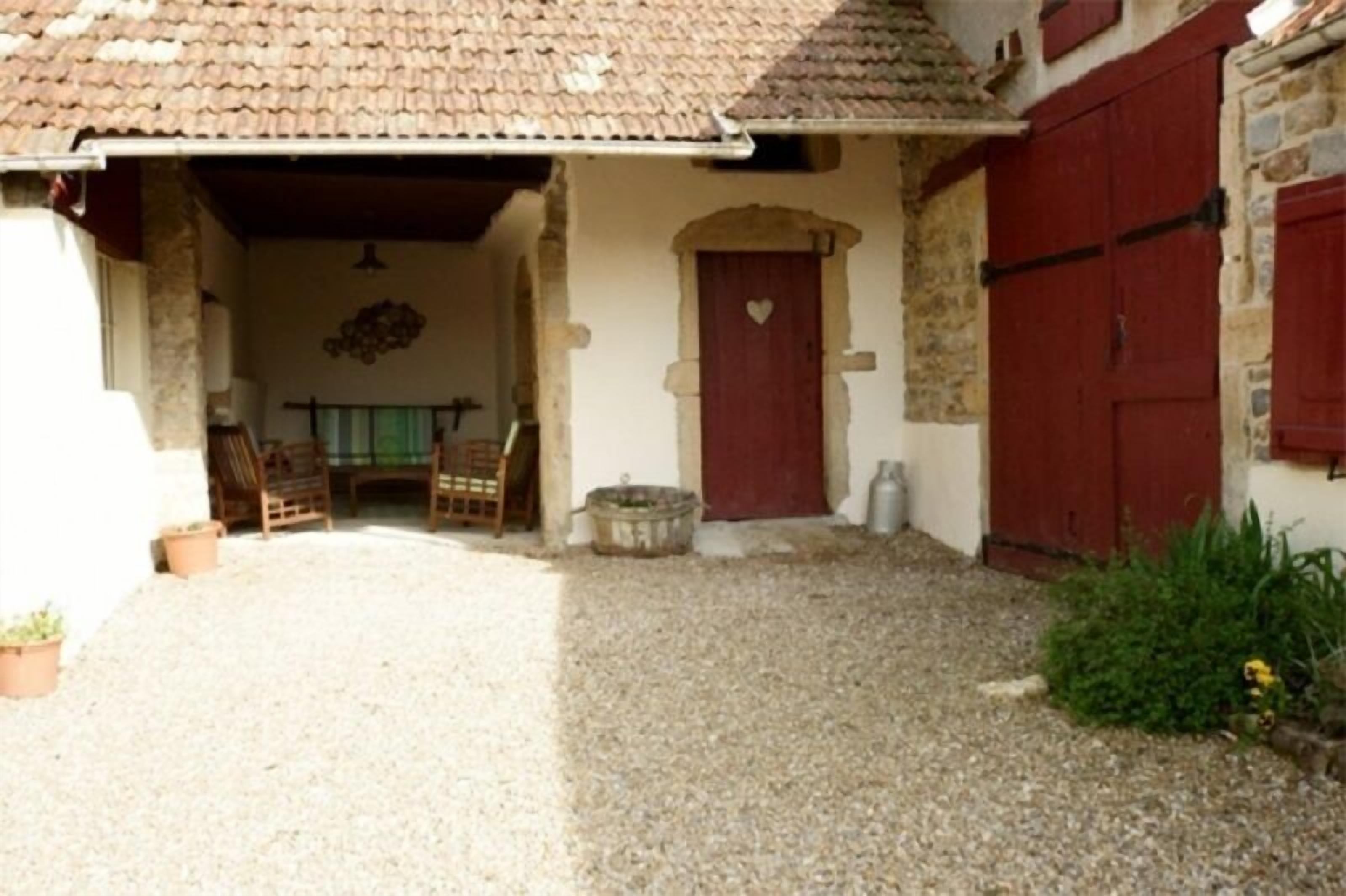 A courtyard with a gravel floor, a wooden chair, a table, and a red door with a heart symbol.