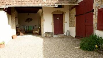 A courtyard with a gravel floor, a wooden chair, a table, and a red door with a heart symbol.