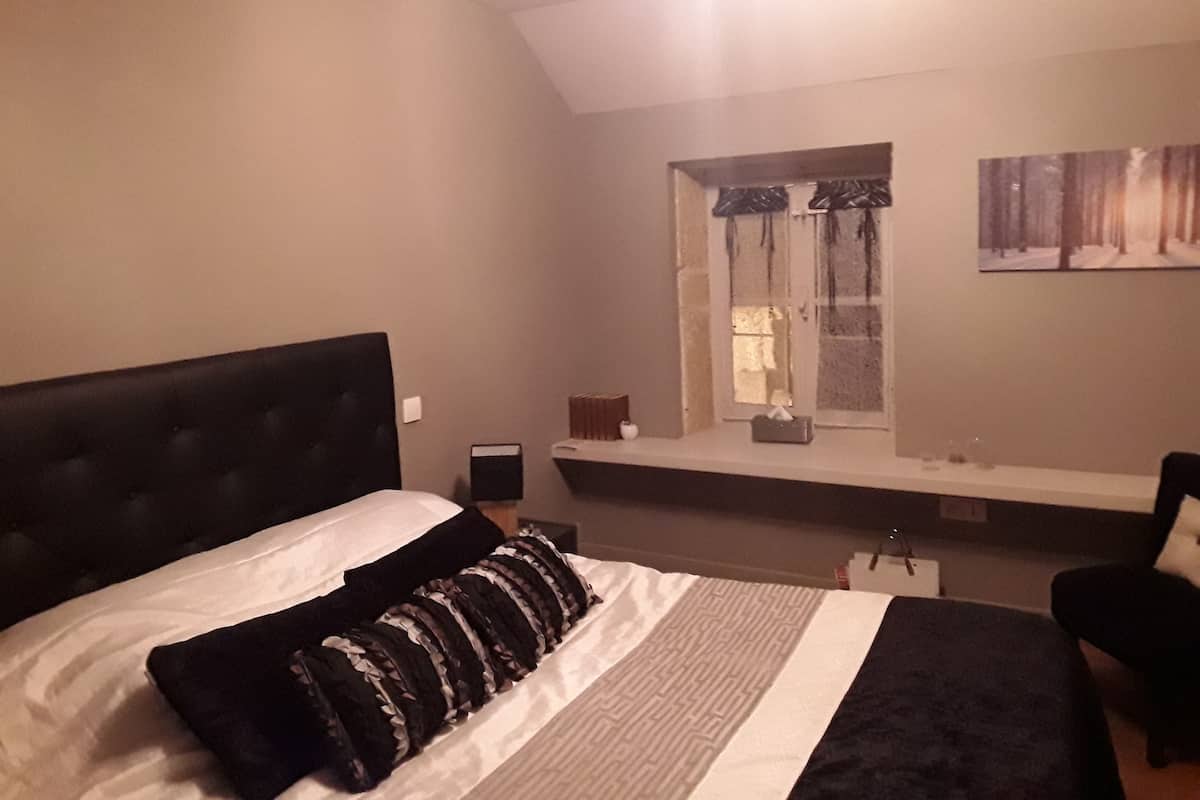 Une chambre à coucher avec un grand lit, une fenêtre avec des rideaux, une table de chevet et une chaise.