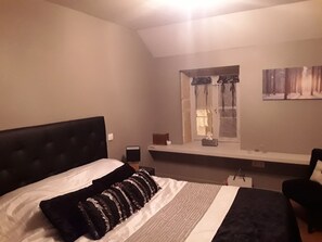A bedroom with a large bed, a window with curtains, a bedside table, and a chair.