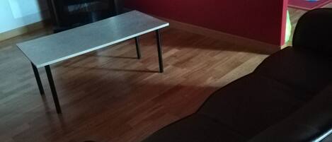 Una sala de estar con un sofá marrón, una mesita y un televisor al fondo.
