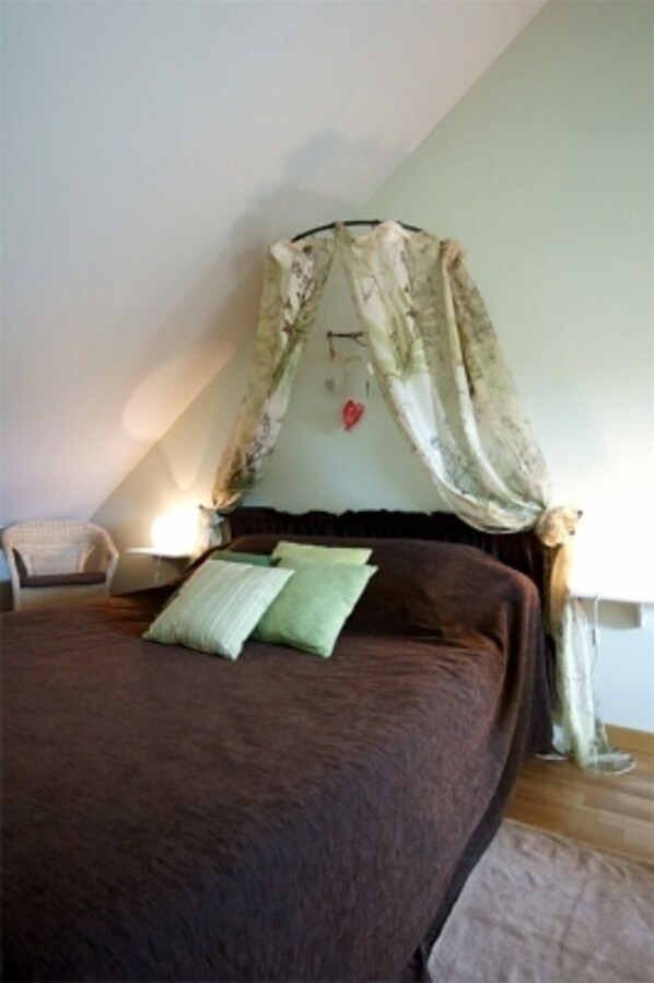 Un dormitorio con una cama grande, una silla, una mesita de noche y un dosel.