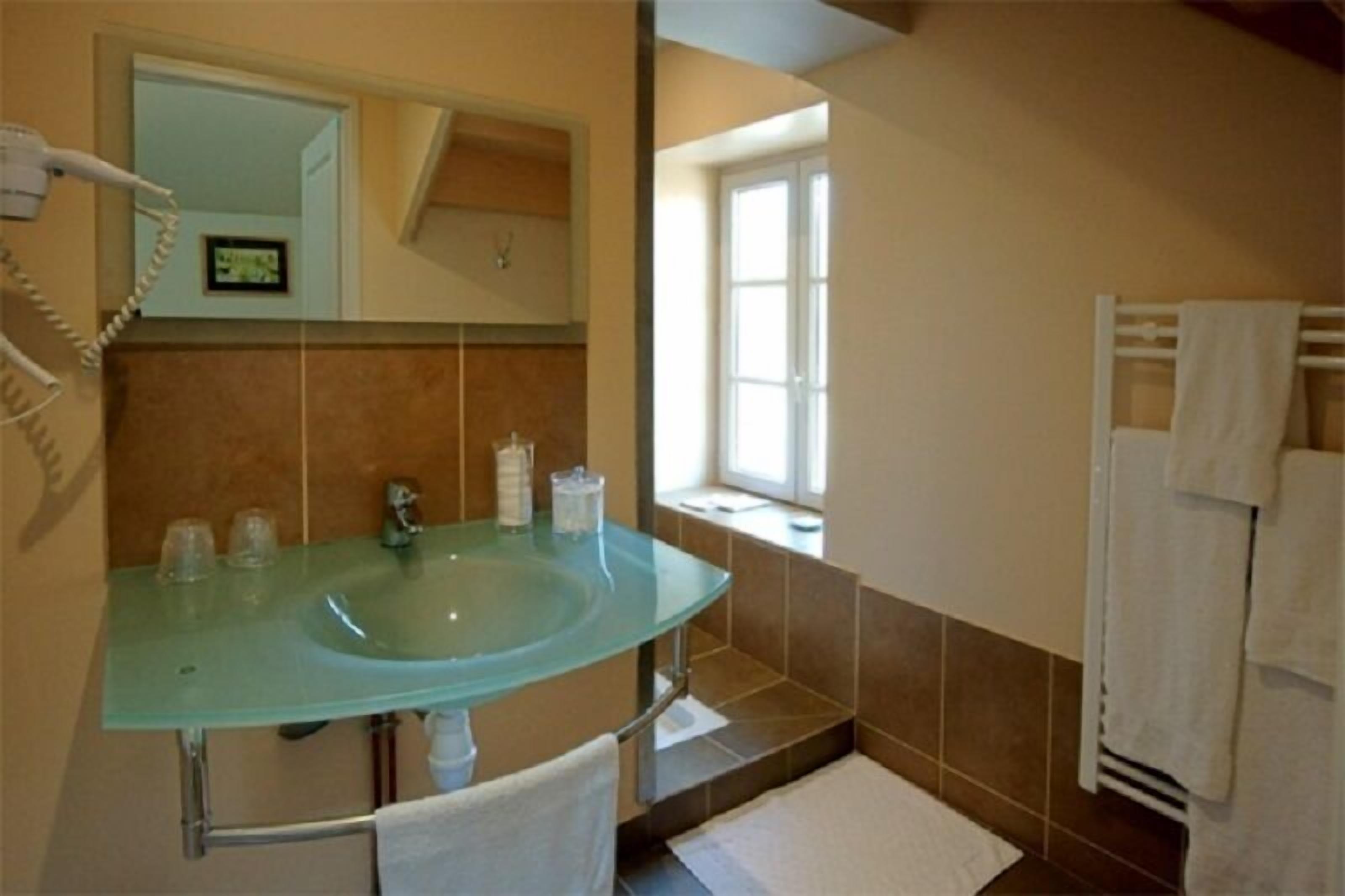 A bathroom with a glass sink, a towel rack, and a window providing natural light.