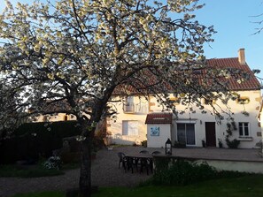 A traditional house with a tiled roof, a garden with a table and chairs, and a tree with white blossoms.
