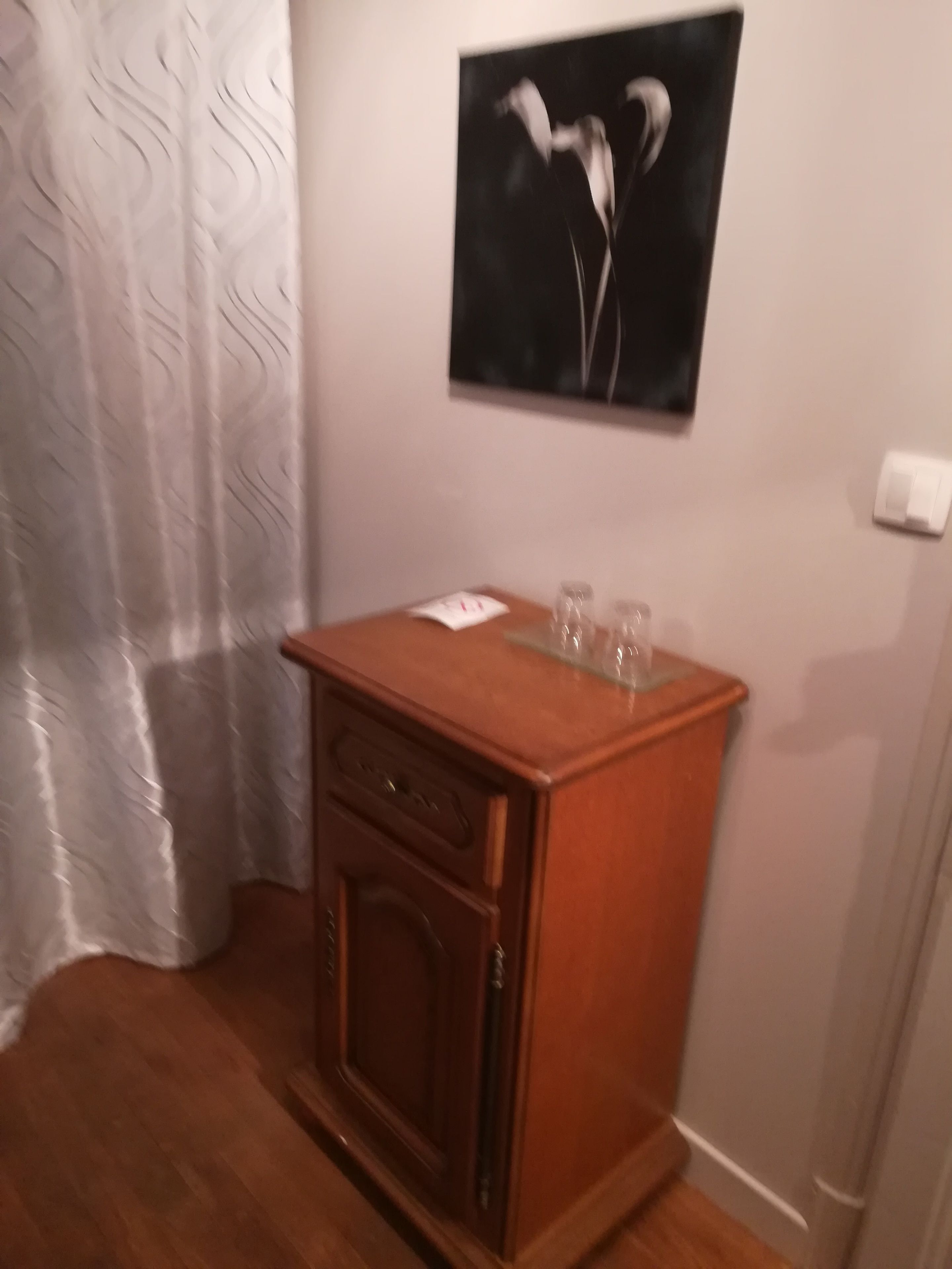 Een hoek van een kamer met een houten kast, een lijst met een foto aan de muur en een kamerbreed gordijn.