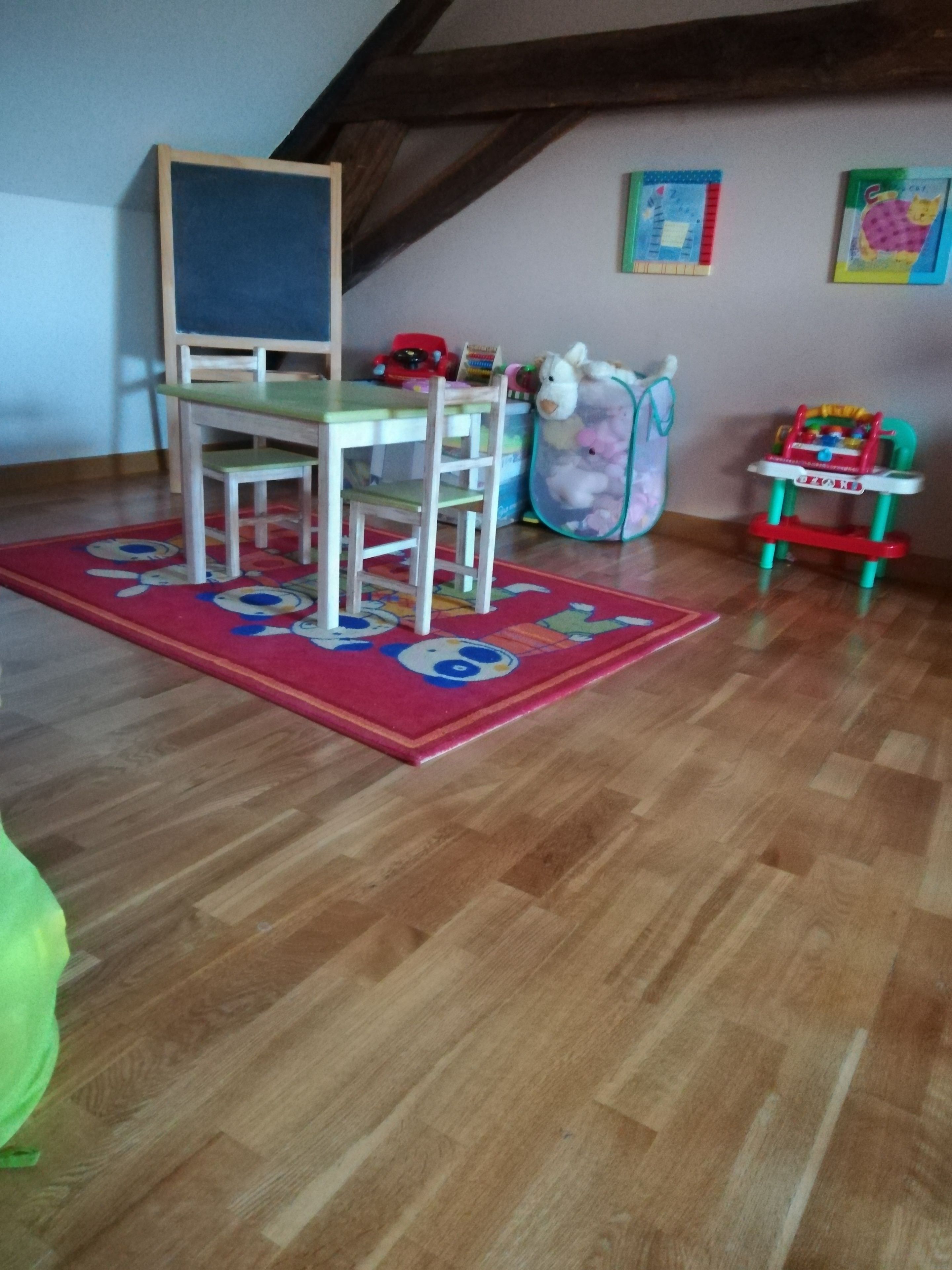 A room with a wooden floor, a green and white chair, a red and white toy car, and a colorful rug.