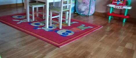 A room with a wooden floor, a green and white chair, a red and white toy car, and a colorful rug.